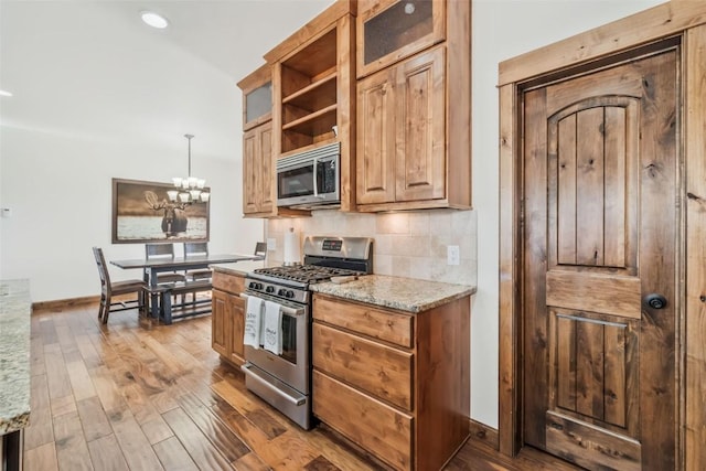 kitchen featuring wood finished floors, a chandelier, light stone countertops, and stainless steel appliances