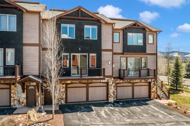 multi unit property with a garage, a balcony, driveway, and stone siding
