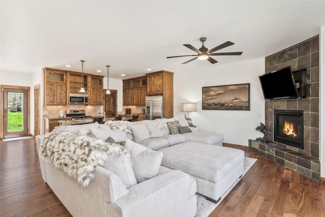 living area with a tiled fireplace, a ceiling fan, recessed lighting, and dark wood-style floors