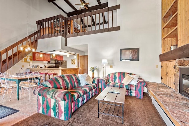 carpeted living area with a stone fireplace, ceiling fan, a high ceiling, and stairs