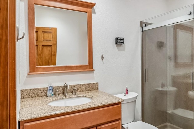 bathroom with a stall shower, vanity, toilet, and a textured wall