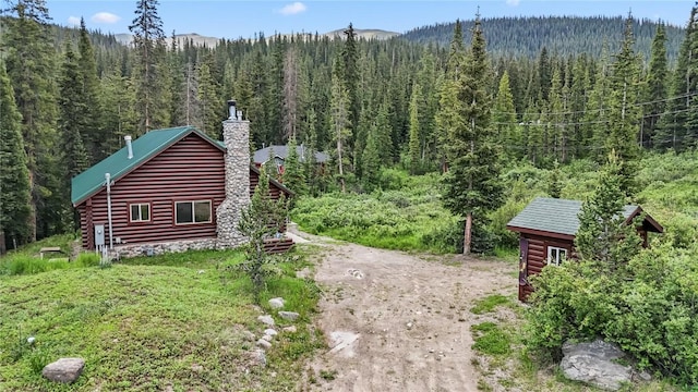 view of side of property with a forest view, a chimney, and driveway