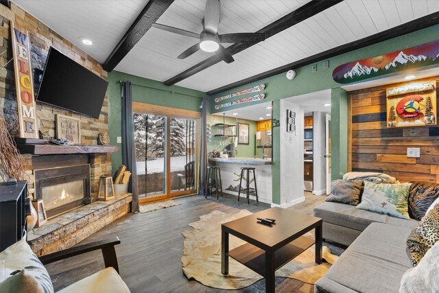 living area with beam ceiling, a ceiling fan, wood finished floors, wooden ceiling, and a fireplace