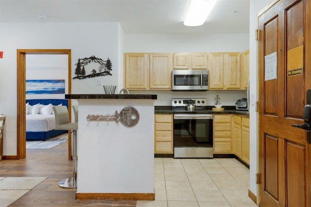 23110 US Highway 6 Unit 5074, Keystone, CO 80435 - kitchen featuring stainless steel appliances, light brown cabinetry, dark countertops, a peninsula, and light wood-style flooring