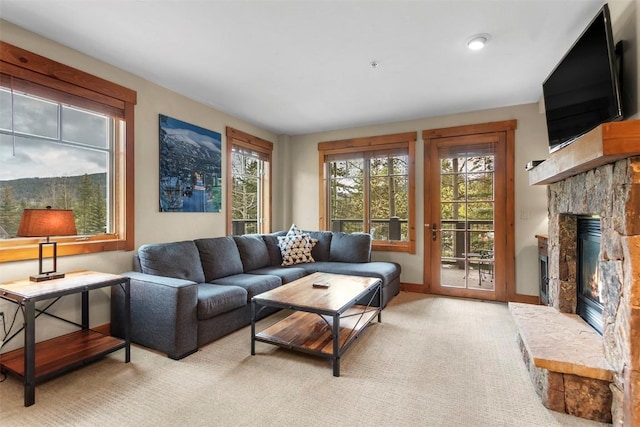 living area featuring a stone fireplace, baseboards, and light carpet