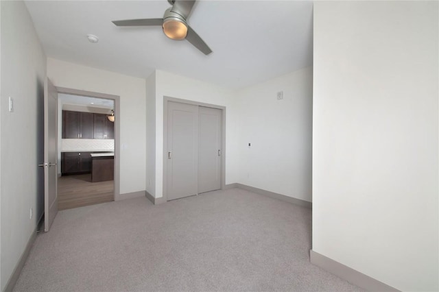 unfurnished bedroom featuring light carpet, baseboards, a closet, and ceiling fan