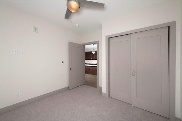 unfurnished bedroom with ceiling fan, baseboards, a closet, and light colored carpet