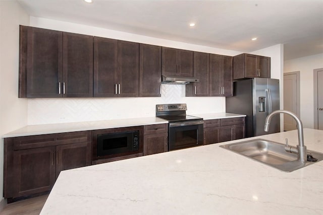 kitchen with under cabinet range hood, dark brown cabinets, a sink, tasteful backsplash, and appliances with stainless steel finishes