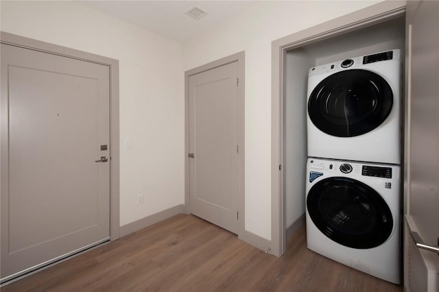 clothes washing area featuring light wood finished floors, laundry area, visible vents, stacked washing maching and dryer, and baseboards