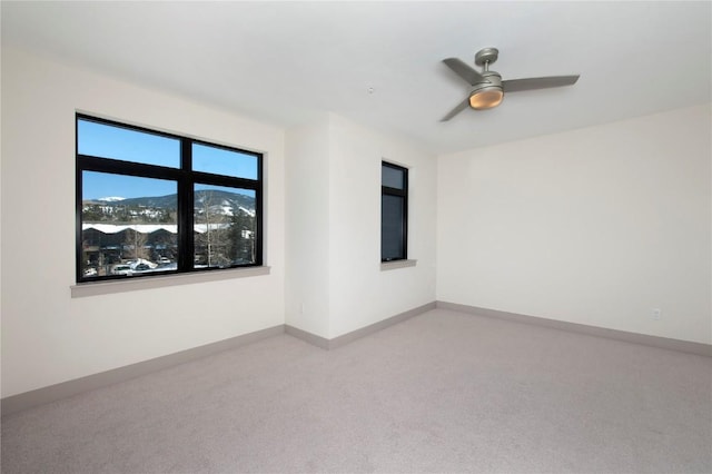 carpeted empty room with a ceiling fan and baseboards