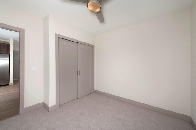 unfurnished bedroom with stainless steel fridge, baseboards, light colored carpet, a ceiling fan, and a closet