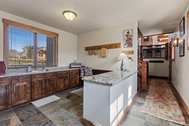 34 Snow Peak Ct, Dillon, CO 80435 - kitchen with stone tile flooring, a peninsula, dark brown cabinets, light stone counters, and a sink