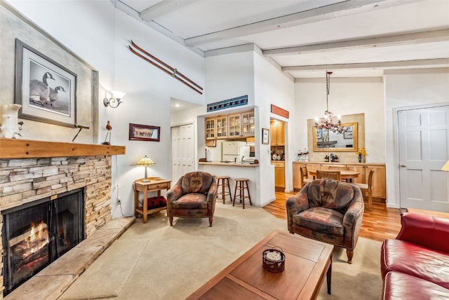 living room with beamed ceiling, light hardwood / wood-style floors, a stone fireplace, and an inviting chandelier