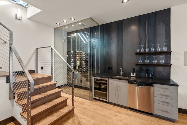 bar with sink, beverage cooler, stainless steel dishwasher, and light wood-type flooring