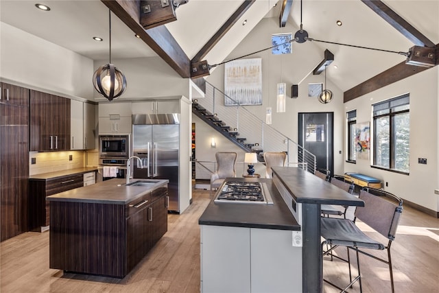 kitchen with decorative backsplash, beam ceiling, built in appliances, a center island with sink, and hanging light fixtures