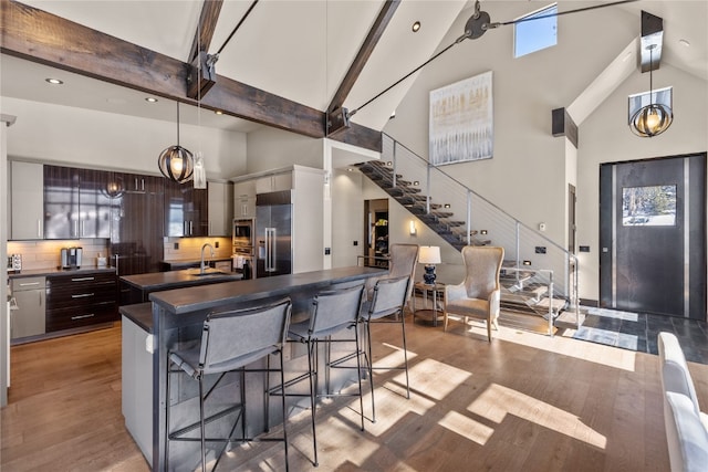 kitchen with decorative backsplash, a kitchen bar, dark brown cabinetry, pendant lighting, and high vaulted ceiling