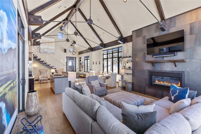 living room featuring beamed ceiling, light wood-type flooring, high vaulted ceiling, and a tile fireplace