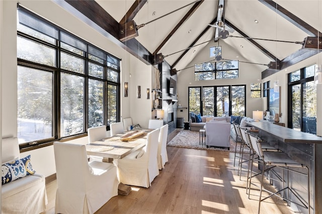 dining room with ceiling fan, light hardwood / wood-style flooring, beamed ceiling, and high vaulted ceiling