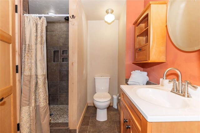 bathroom featuring tile patterned floors, vanity, baseboards, a tile shower, and toilet