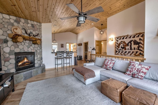 living area with lofted ceiling, wood finished floors, a stone fireplace, wood ceiling, and ceiling fan