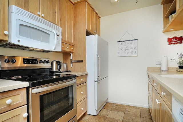 kitchen featuring light countertops, stone finish floor, a sink, white appliances, and baseboards
