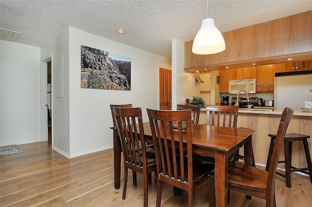 dining space with baseboards, light wood-style floors, and a textured ceiling