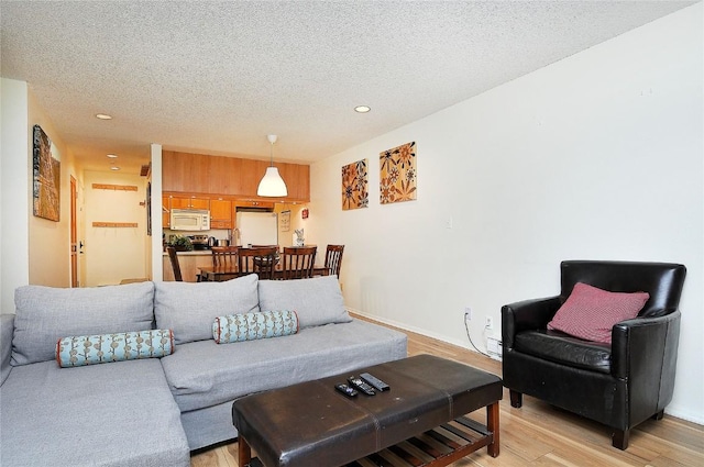 living room featuring light wood-type flooring, baseboards, recessed lighting, and a textured ceiling