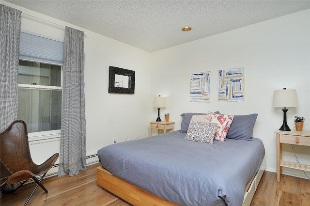 bedroom with baseboards, baseboard heating, wood finished floors, and a textured ceiling