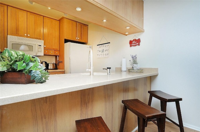kitchen featuring brown cabinets, a peninsula, a breakfast bar, and white appliances