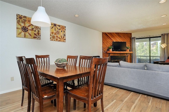 dining space featuring a textured ceiling, light wood-style floors, wooden walls, a fireplace, and recessed lighting