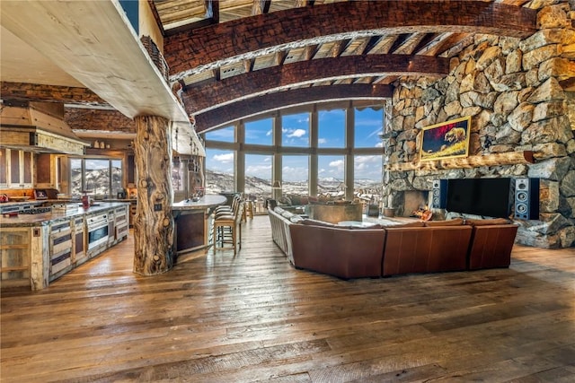 unfurnished living room featuring hardwood / wood-style flooring, plenty of natural light, beam ceiling, and a stone fireplace