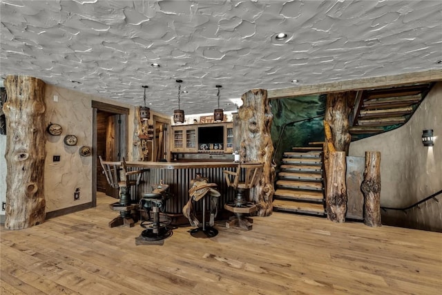 bar with hardwood / wood-style floors, a bar, and stairs