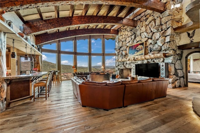 living room featuring wood-type flooring, a stone fireplace, and vaulted ceiling with beams