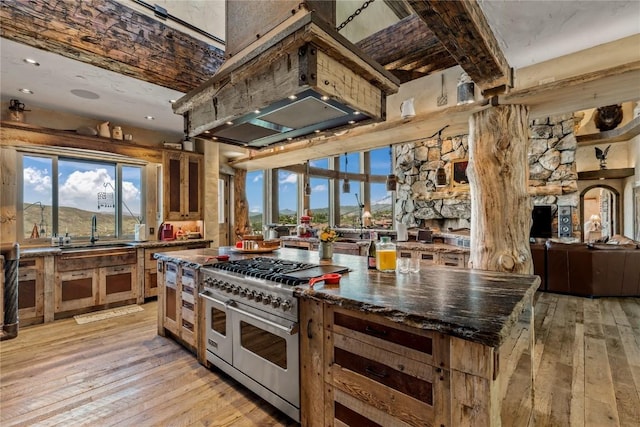 kitchen featuring range with two ovens, a sink, ventilation hood, a center island, and light wood finished floors