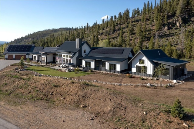 403 Revett Dr, Breckenridge, CO 80424 - view of front of home with roof mounted solar panels, a garage, a chimney, board and batten siding, and a view of trees