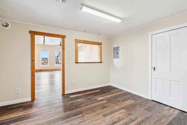 empty room featuring electric panel, crown molding, wood finished floors, and baseboards