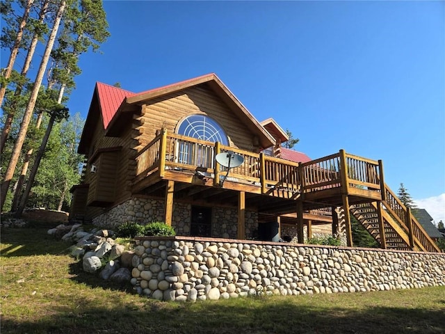 rear view of house featuring log exterior, stone siding, metal roof, and a deck