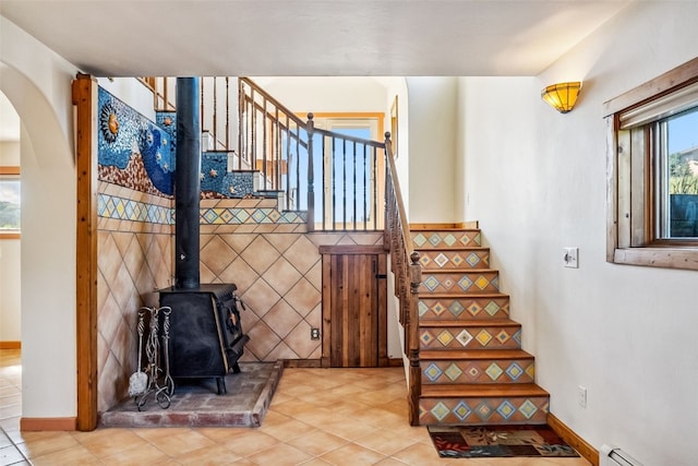stairs featuring a baseboard heating unit, tile patterned floors, arched walkways, baseboards, and a wood stove