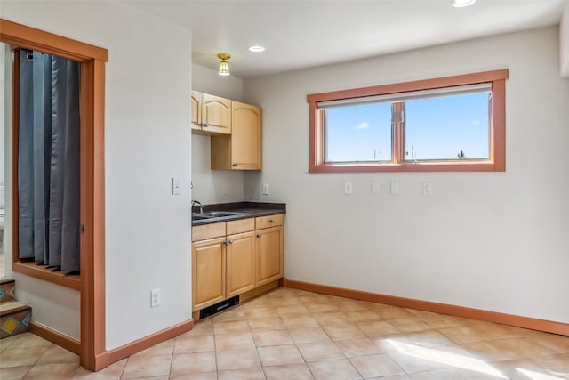 kitchen featuring recessed lighting, dark countertops, light brown cabinets, a sink, and baseboards
