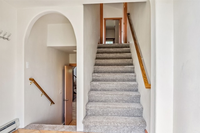 staircase with baseboard heating and arched walkways