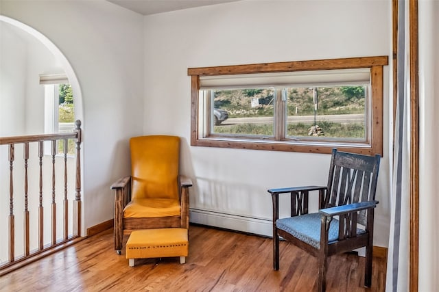 sitting room featuring a baseboard heating unit, baseboards, wood finished floors, and arched walkways