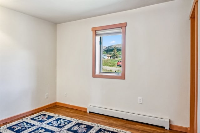 spare room featuring baseboards, wood finished floors, and a baseboard radiator