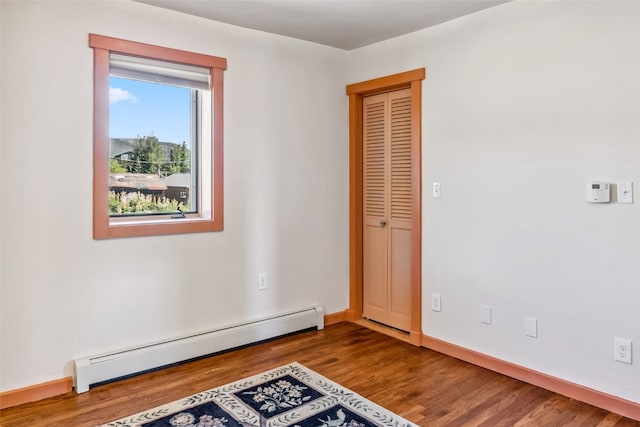 empty room with a baseboard heating unit, baseboards, and wood finished floors
