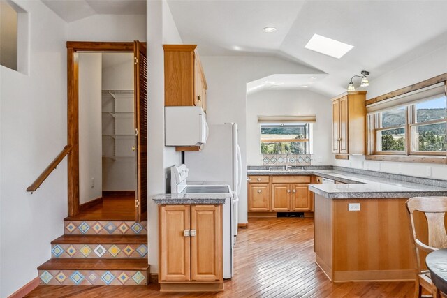 kitchen with white appliances, lofted ceiling with skylight, a sink, and a healthy amount of sunlight