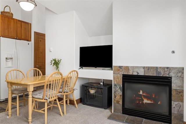 dining area with light colored carpet, a warm lit fireplace, and baseboards