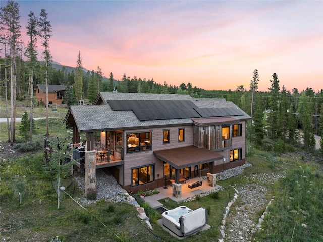 back house at dusk with solar panels, an outdoor hangout area, and a patio