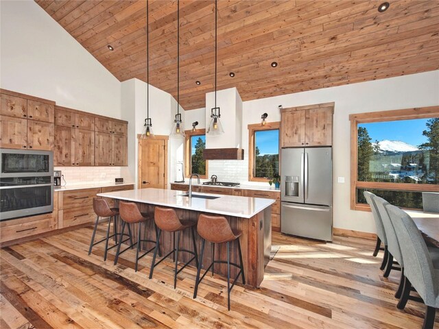 kitchen featuring hanging light fixtures, decorative backsplash, a center island with sink, appliances with stainless steel finishes, and light wood-type flooring