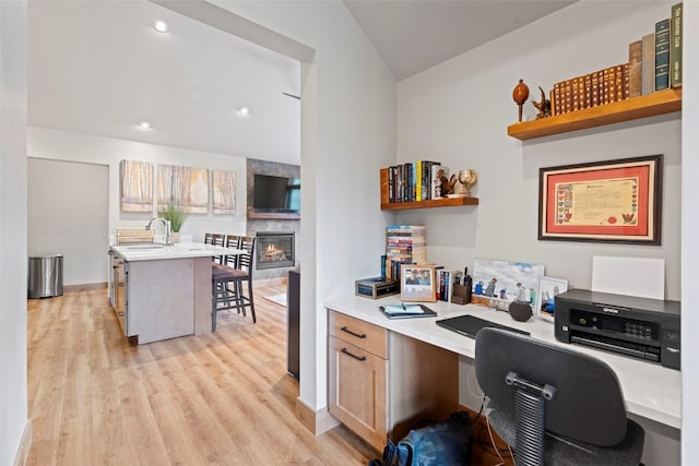 office area featuring sink, a large fireplace, lofted ceiling, and light hardwood / wood-style flooring