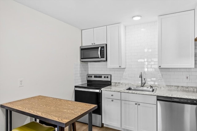 kitchen featuring appliances with stainless steel finishes, a sink, decorative backsplash, white cabinets, and wood finished floors