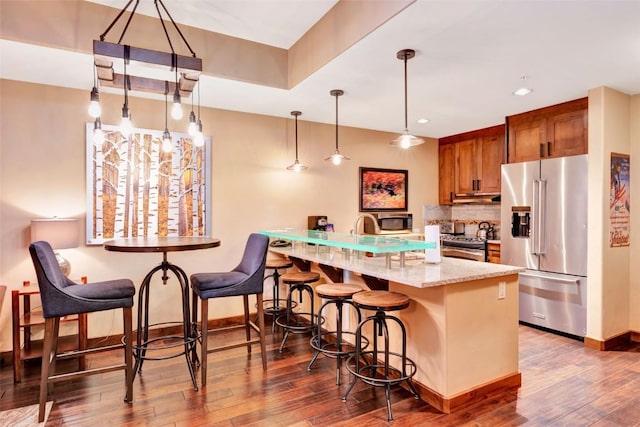 kitchen featuring brown cabinetry, hardwood / wood-style flooring, under cabinet range hood, a breakfast bar, and appliances with stainless steel finishes